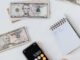 Vue aérienne d'une main utilisant une calculatrice avec des dollars américains et des billets, représentant les finances et la budgétisation.