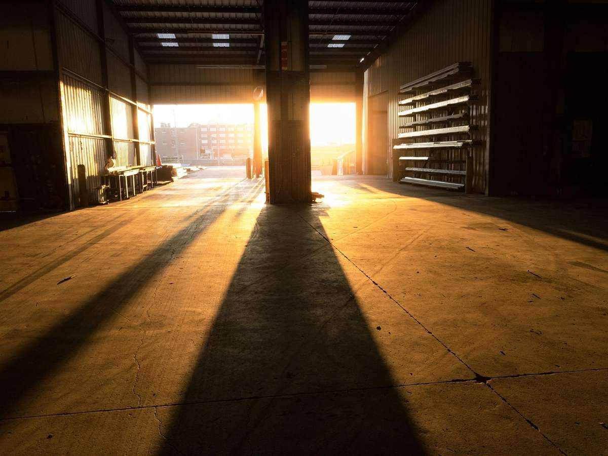 Lumière dorée inonde le hall industriel, projetant de longues ombres sur le béton