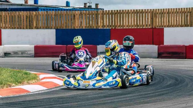 Trois karts dérapent en virage sur circuit, pilotes en casques colorés