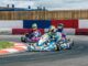 Trois karts dérapent en virage sur circuit, pilotes en casques colorés