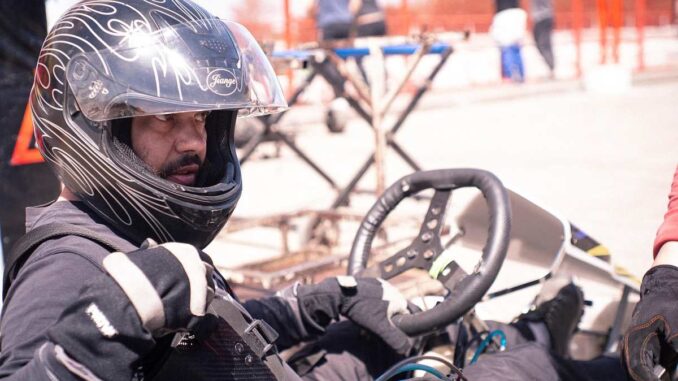 Un homme en karting, casque noir, mains sur le volant, prêt à conduire